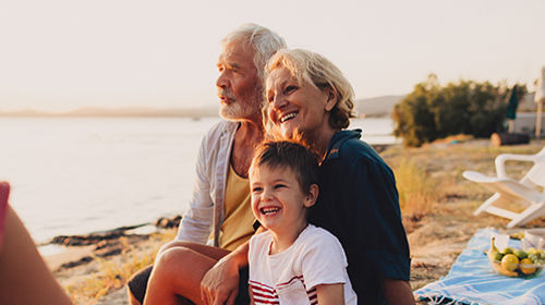 Older couple and a smiling child sit together by a lakeside.