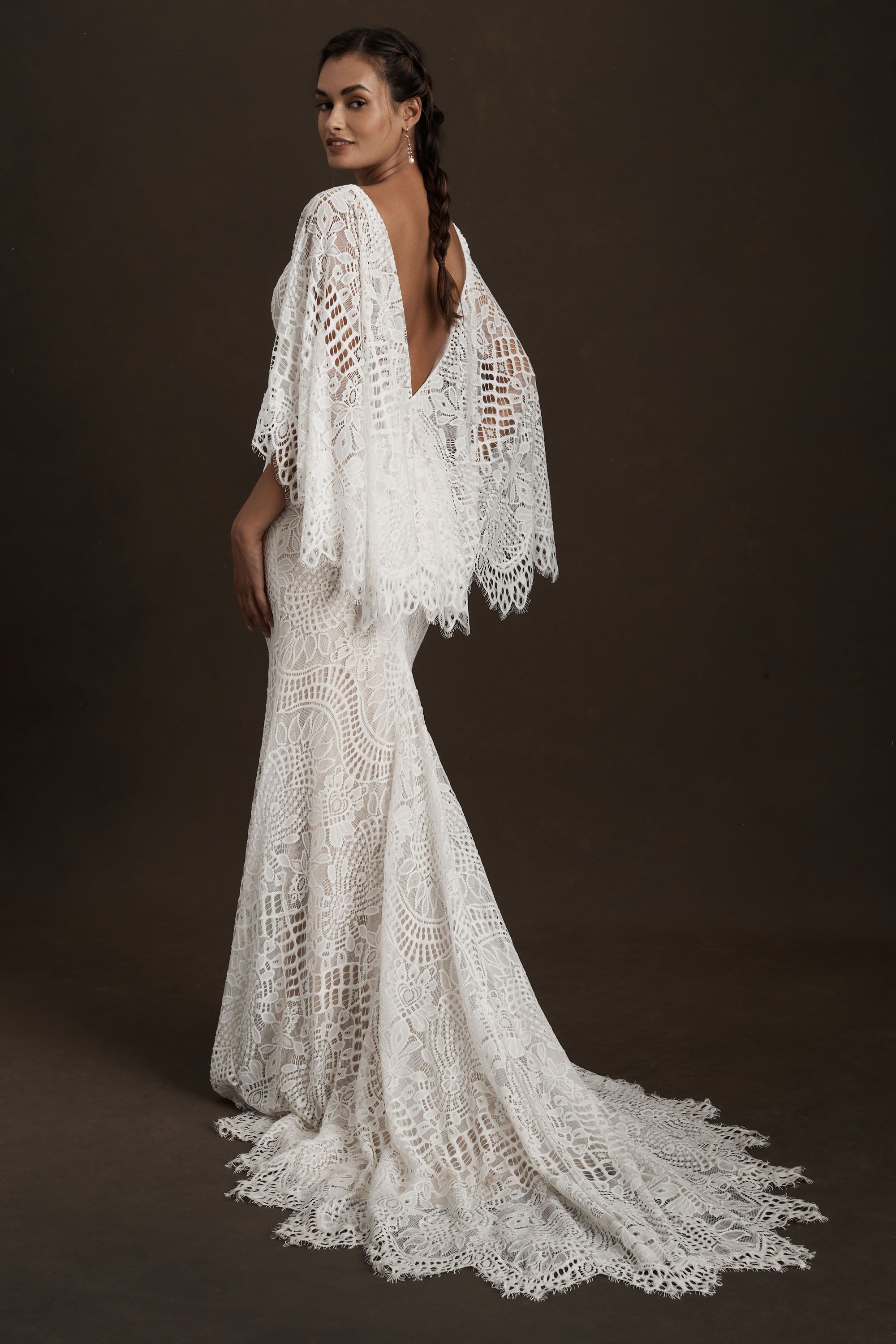 Made from intricate graphic lace, this fitted gown features a plunging v-neckline and dramatic train. The cascading flutter sleeves transform into a gorgeous cape detail to frame the open back