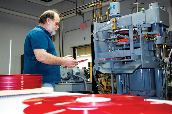 An image shows a man who presses records inspecting a recently pressed LP.
