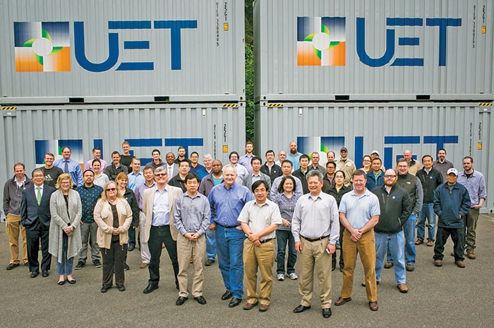 A group of UniEnergy Technology scientists and engineers pose in front of four shipping containers housing flow batteries.