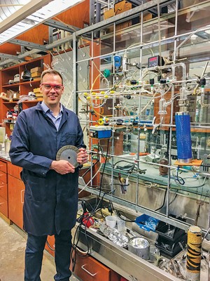 Eric Schelter stands in a chemistry lab holding a plate-sized magnet.