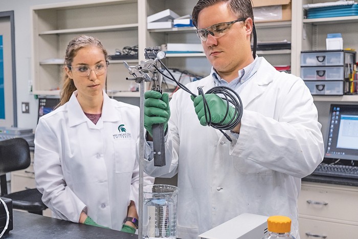 Photo of a researcher holding electrodes over a beaker of water.
