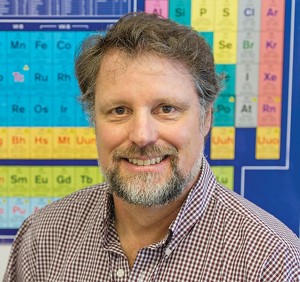 Headshot of Chris Palmer in front of a colorful periodic table.