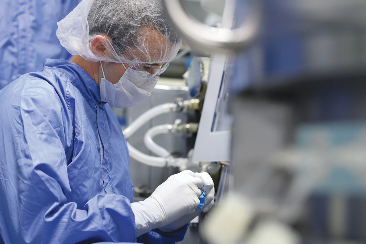 A photograph of a worker in full protective garb adusting a processing vessel at a vaccine maufactuirng plant.