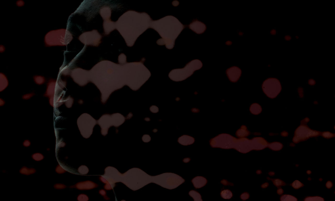 Red spots of protein produced by a 2D gel superimposed on the shadowed outline of a human face.