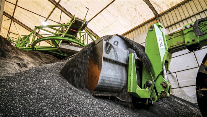 A bulldozer scoops ground tire bits. In the background, the roof of an industrial builiding is visible.