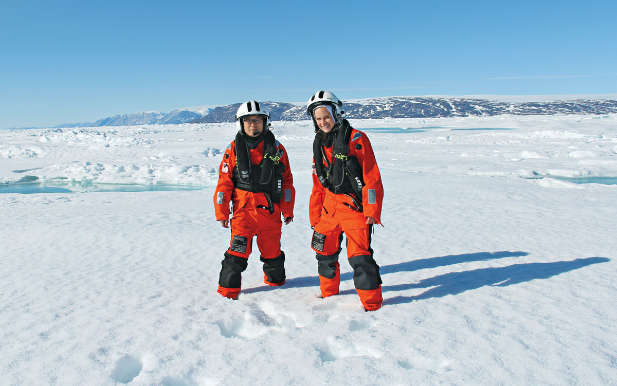 Two people in orange gear and white helmets in the Arctic.