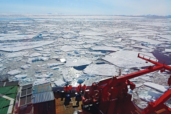 An orange research vessel traveling through icy water.