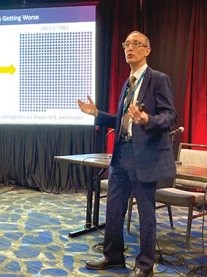 A man giving a presentation in a hotel conference room. The part of the title on a projected slde behind him reads "...getting worse."