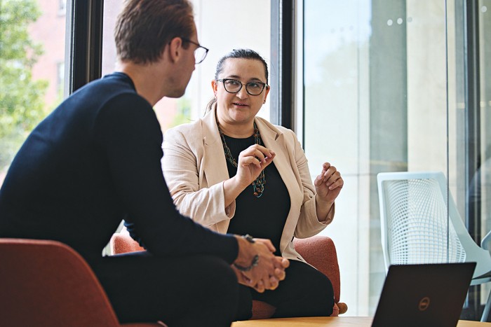 A woman, seated, in conversation with someone whose back is turned to us.
