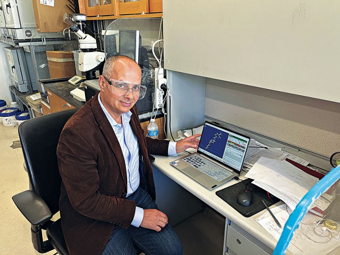 A man seated in a laboratory with computer equipment.