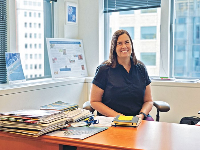 A woman sitting at her desk in an office with a big window.