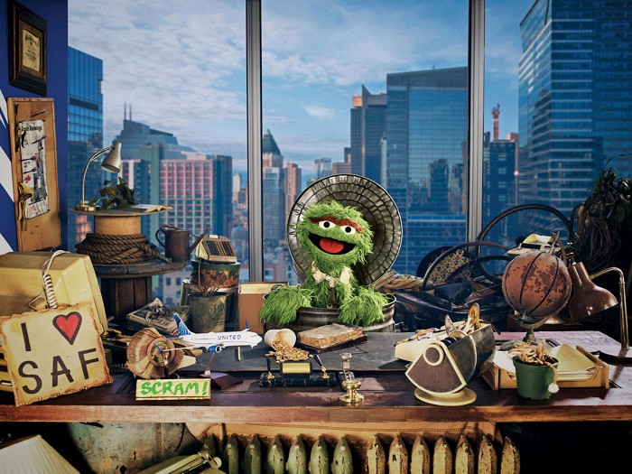 Oscar the Grouch behind a desk in an office laden with the detritus of modernity.