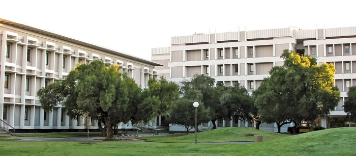 An image of two buildings. There are some trees and small hillls obscuring the buildings.