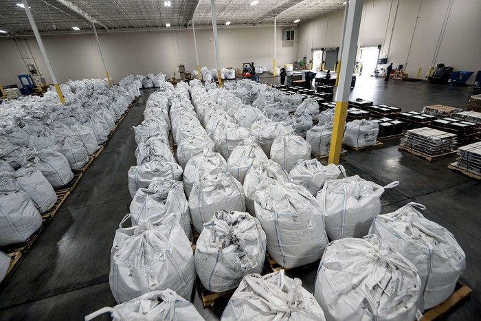 Several rows of white, garbage-can-size sacks filled with black powder inside a warehouse.