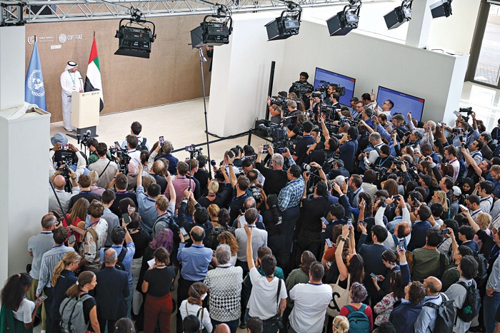 COP28 director-general Majid Al Suwaidi, wearing a long white robe and head covering, speaks to a group of about 200 members of the press in Western clothing from a podium at the COP 28 meeting in Dubai, United Arab Emirates.