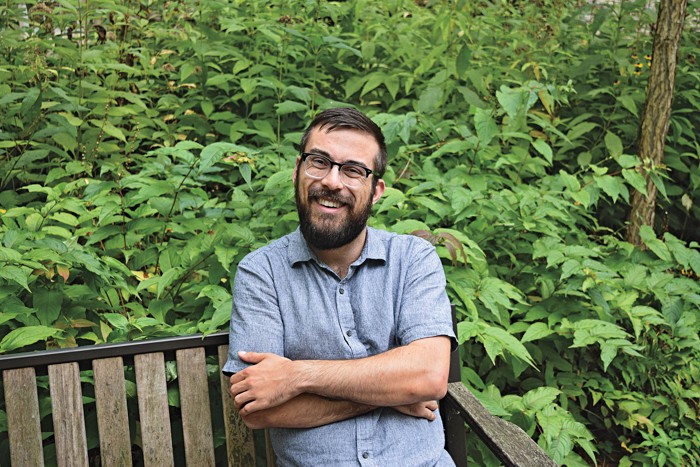 A scientist sitting on a bench outside while smiling at the camera.