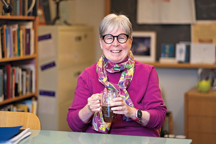 Michelle Francl, a chemist with a gray pixie haircut, wearing thick-rimmed glasses, a turtleneck, and a scarf, sits in an office with a mug of tea.