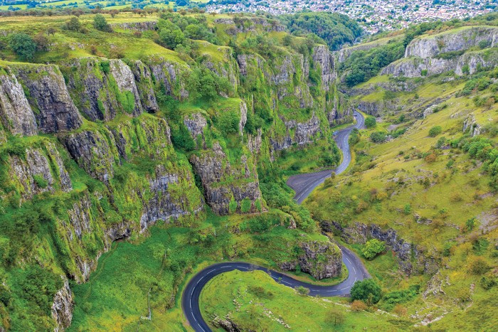 Steep cliffs topped with green vegetation surround a winding river at Cheddar Gorge.