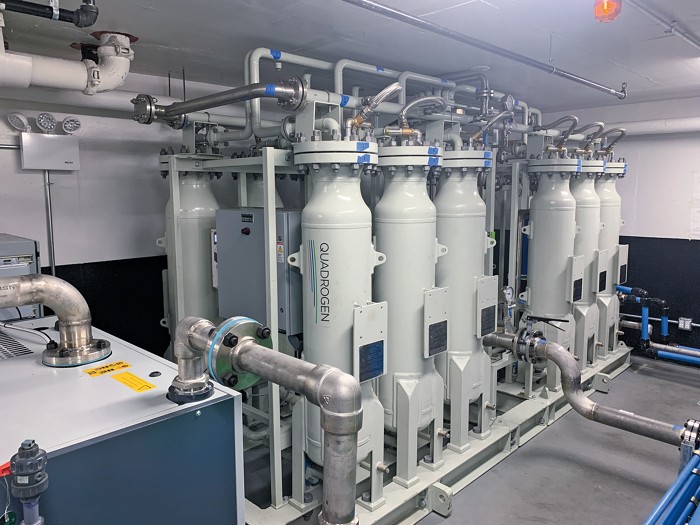 Two rows of six tanks, each about 2 m tall, are housed in an equipment room.