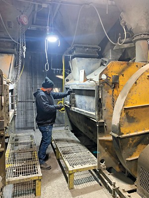 A person operates a sliding door on a large mixing machine in a factory.