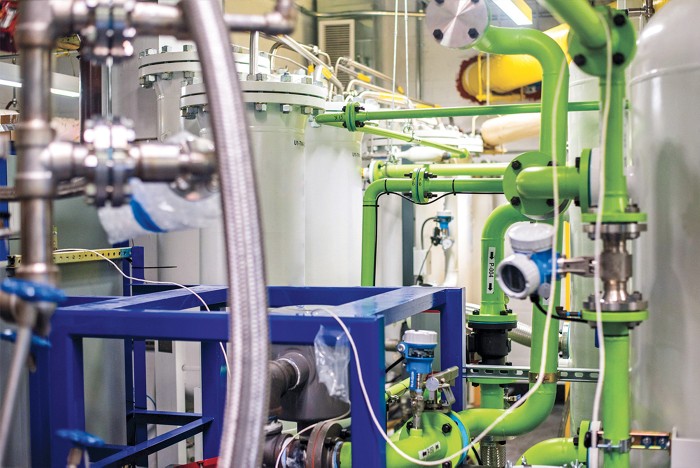 A clean, new equipment room with silver hoses, white tanks, blue scaffolds, and yellow pipes.