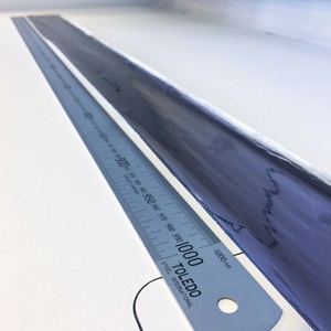 A meter-long ruler sits next to a long strip of flexible plastic coated in a black film.