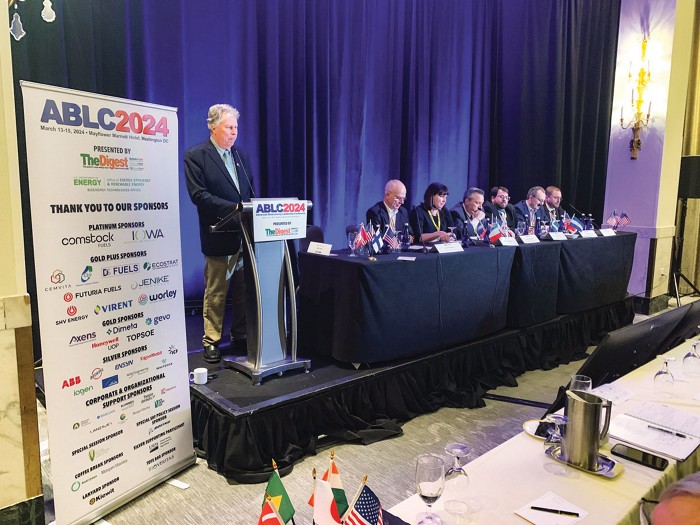 One person at a podium and six people seated for a panel discussion at a conference.