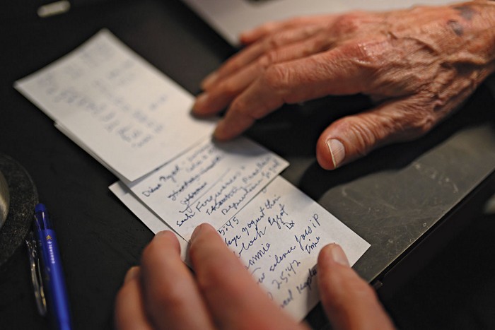 Three sticky notes laid out on a table, scrawled with handwritten notes and framed by two wizened hands.