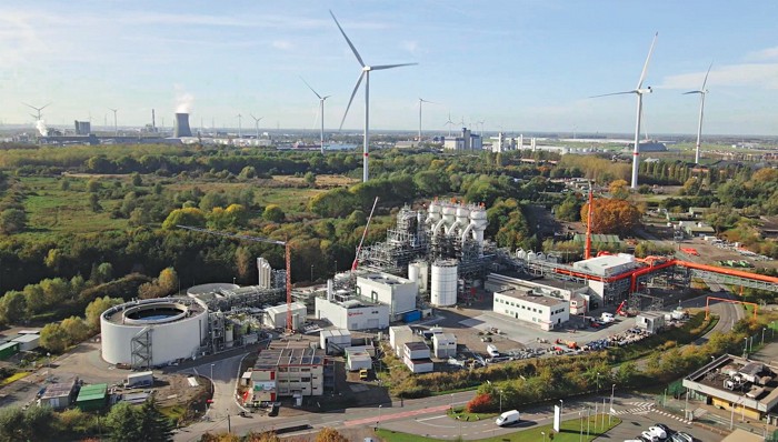 Several wind turbines and a nuclear power plant stand behind a large steel factory in Belgium.