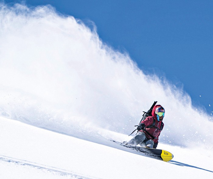 A person in a red jacket skis down a mountain covered in powdery snow.