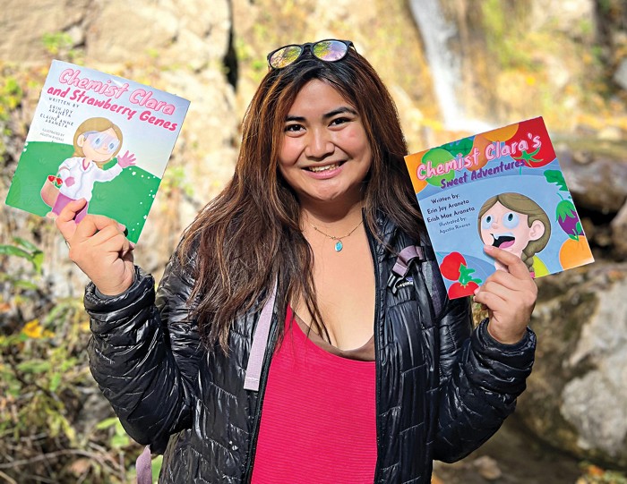 Woman holding children's picture books in her hands with rocks in the background.