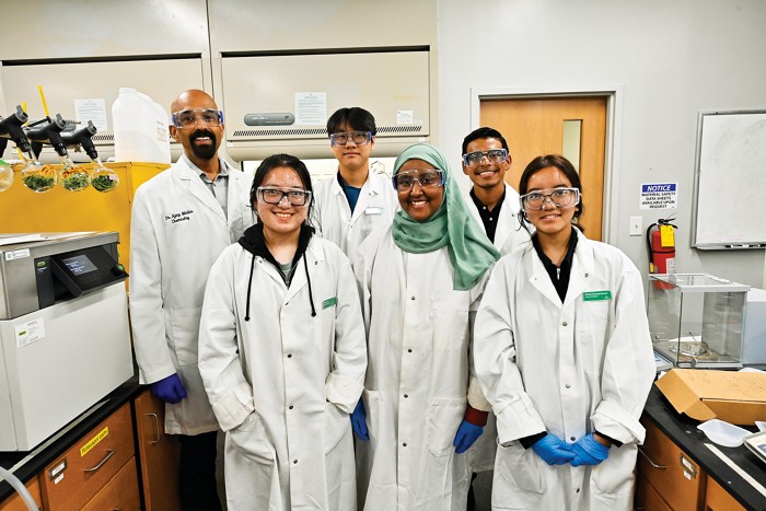 A group of six people stand together in a lab, smiling.