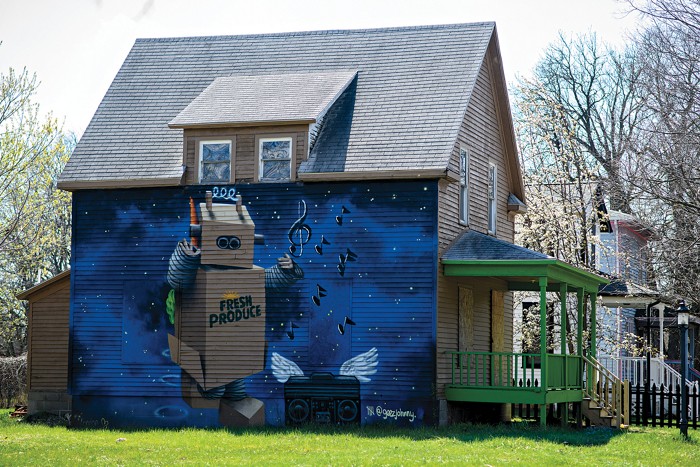 A mural on a house features a robot with "Fresh produce” on its middle. It’s standing next to a boombox with wings and music notes floating up against a blue background.