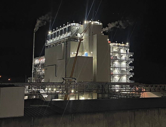 A chemical plant at night. There are large lights, and the facility is housed inside a large white building. 