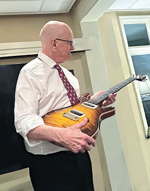 A photo of K. Barry Sharpless holding a guitar.