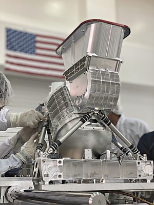 Researchers lay gloved hands on a large, silver machine.