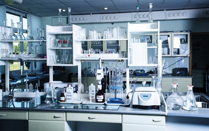 A laboratory bench stocked with trays of labeled bottles of chemicals, shelves filled with clean lab glassware, and a centrifuge.
