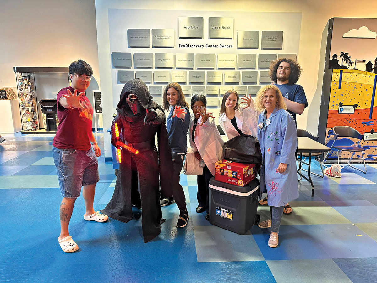 A group of seven smiling volunteers stand together. One is dressed as Darth Vader.
