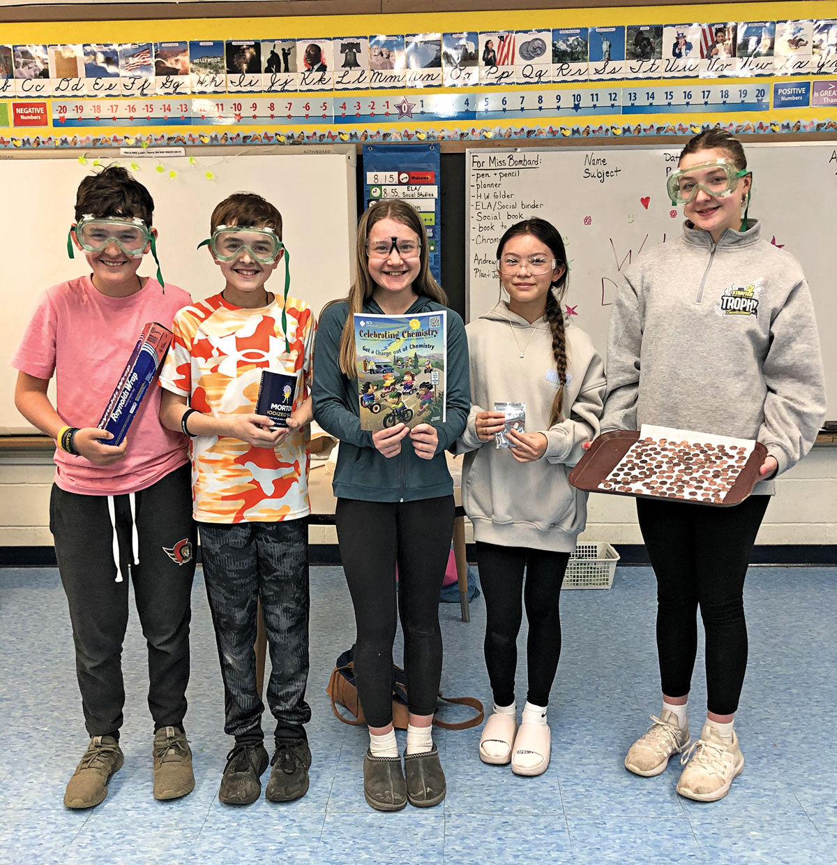 Five smiling children in goggles hold up equipment for making coin batteries.