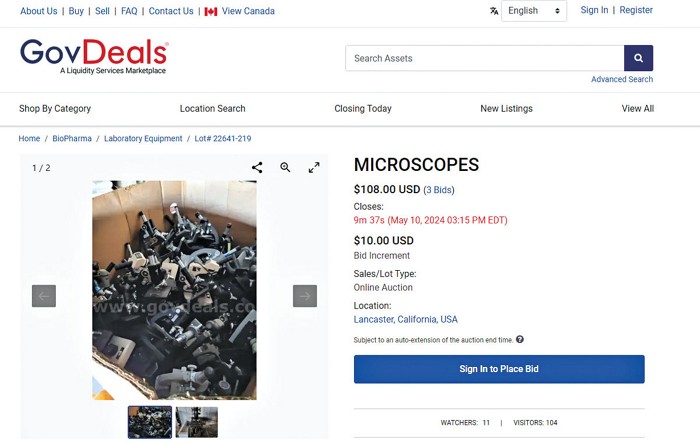A screenshot from the auction website GovDeals shows a listing in the Laboratory Equipment category Microscopes. A photo shows a jumble of a dozen or more simple light microscopes in a warehouse-scale cardboard box. The listing had received three bids and was at $108 when the screenshot was taken.
