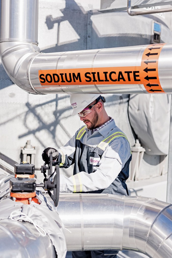 A man working in Evonik Industries silica plant in Charleston, South Carolina. He is wearing protective gear and working near a pipe that says 