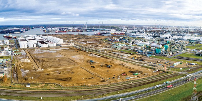 A large piece of land is cleared down to fresh dirt. In the background there is a tank farm.