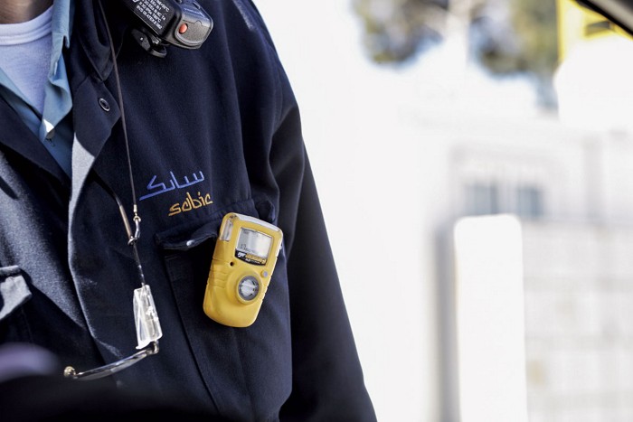 A close-up of an operator at a Sabic plant. The person is wearing a uniform with a sensor pinned to it.