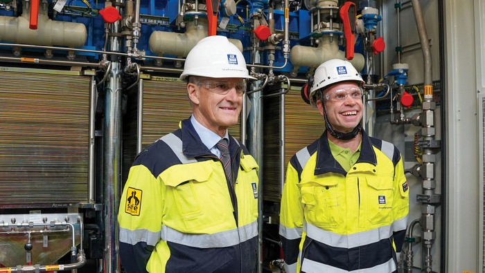 Norwegian prime minister Jonas Gahr St?re and Yara CEO Svein Tore Holsether pose in front of an electrolyzer.