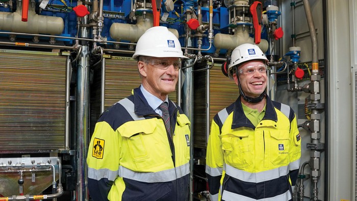 Norwegian prime minister Jonas Gahr Støre and Yara CEO Svein Tore Holsether pose in front of an electrolyzer.