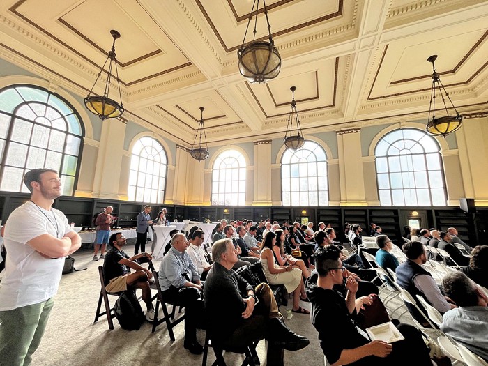 A crowd of people sit in folding chairs while looking toward the front of a large room.