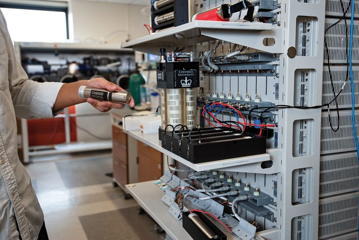 Someone holds a silver, cylindrical battery in a laboratory.