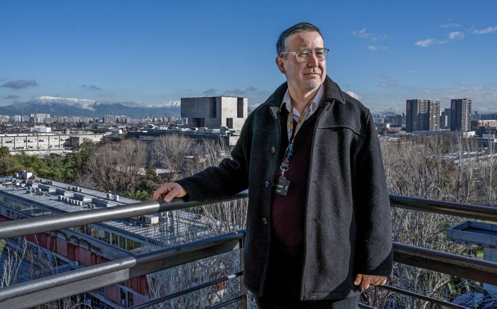 Pablo Pastén poses near the edge of a railling overlooking the city skylline.