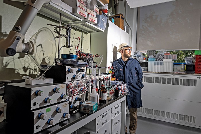 Alán Aspuru-Guzik stands in his research lab. Scientific equipment can be seen on a lab bench in the foreground.